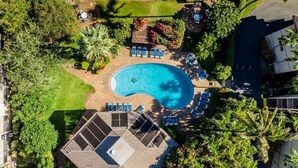 An aerial view of a swimming pool with lounge chairs and a covered seating area, surrounded by greenery and a building. - Beautiful Kihei Condo with Ocean & Haleakala Mountain Views (Kihei)
