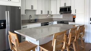 Una cocina moderna con armarios blancos, electrodomésticos de acero inoxidable, una isla central con sillas y un ventilador de techo.