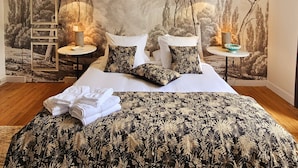 A bedroom with a large bed, two nightstands, and a mural of trees. There are two black pendant lamps on the nightstands.