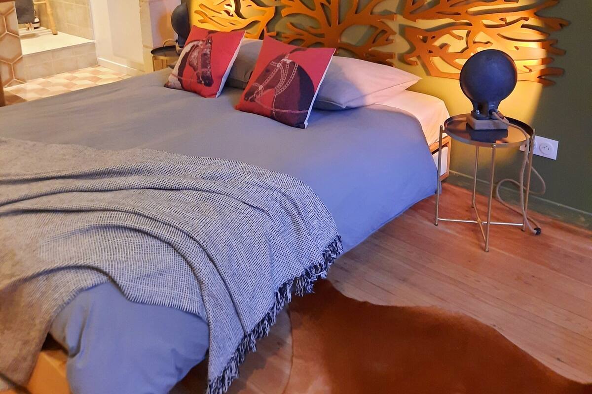 Une chambre à coucher comprenant un lit, une tête de lit décorative, une petite table avec une lampe et un mur orné d’un motif texturé.