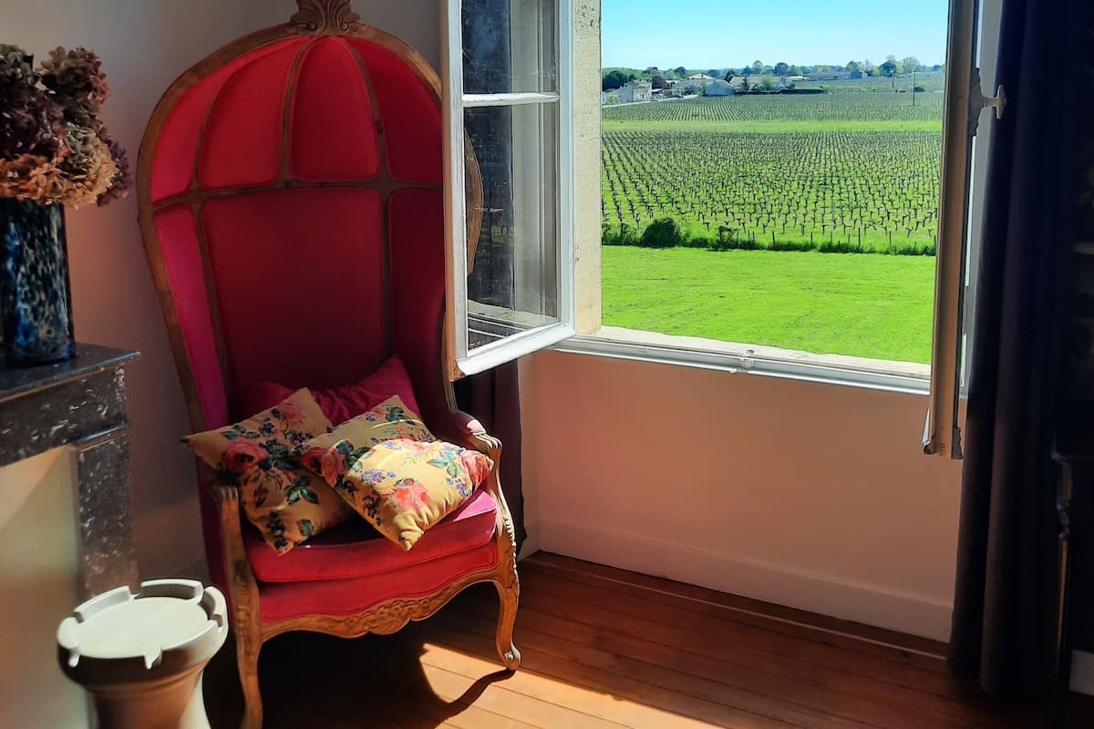 Une pièce avec une chaise rouge près d’une fenêtre donnant sur un champ verdoyant.