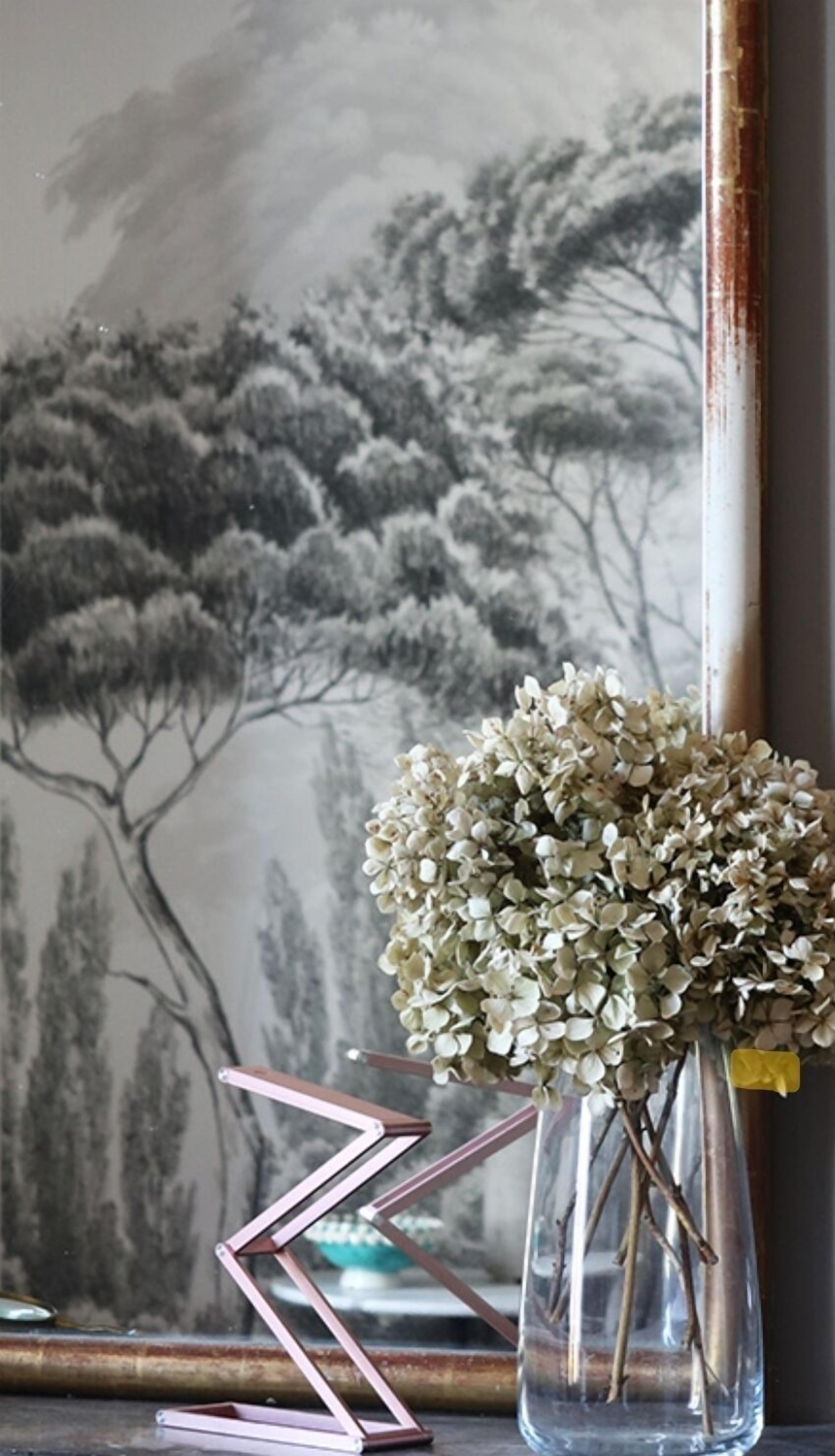 Un vaso con fiori bianchi su un tavolo, un dipinto raffigurante alberi e una scultura in metallo.