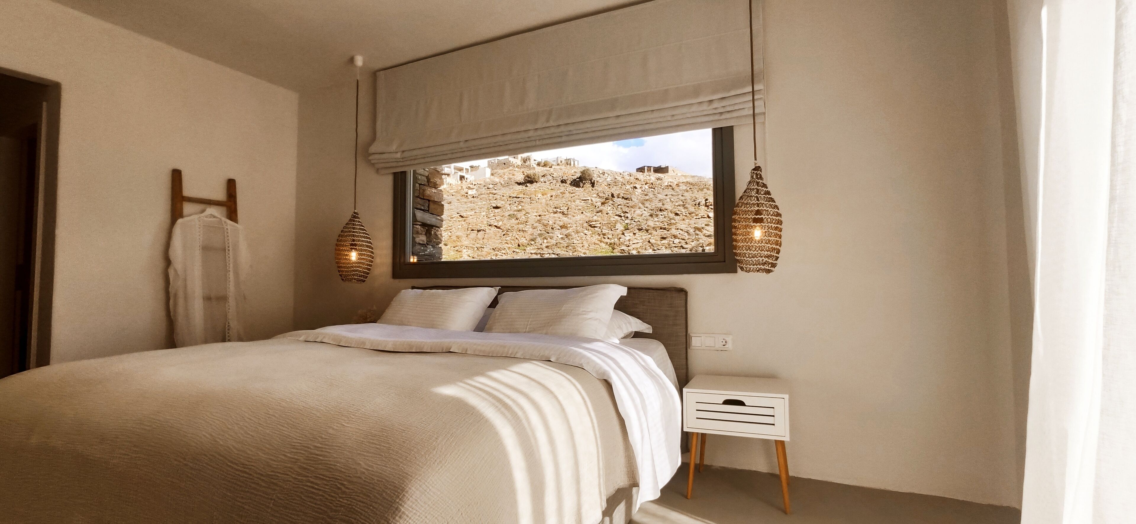 A bedroom with a bed, a nightstand, a window with a view of a rocky landscape, and two wall-mounted lamps.