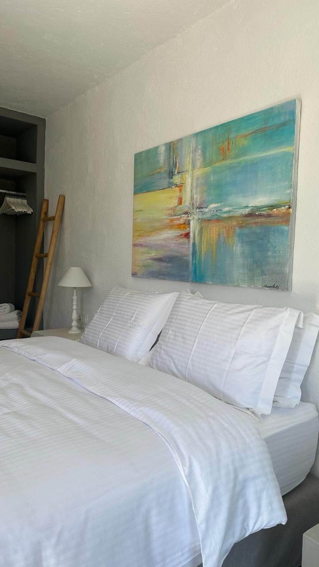 A neatly made bed with white linens in a room with a large abstract painting on the wall.