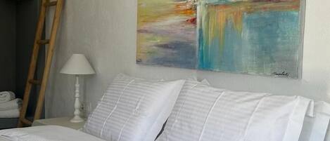 A neatly made bed with white linens in a room with a large abstract painting on the wall.