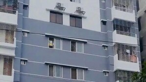 A multi-story residential building with a gated entrance, air conditioning units, and a parked car.