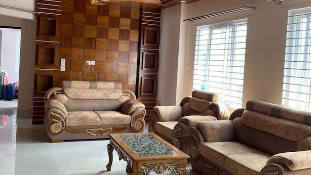 A spacious living room with a high ceiling, wooden paneling, and a ceiling fan. There are two sofas and a coffee table.