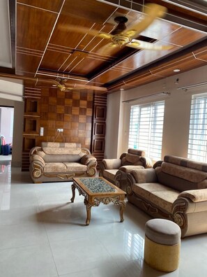 A spacious living room with a high ceiling, wooden paneling, and a ceiling fan. There are two sofas and a coffee table. - 4 Beds Condo Holiday Home at Bashundhara, Dhaka (Dhaka)
