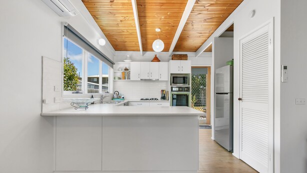 A modern kitchen with white cabinetry, a wooden ceiling, and a large island.