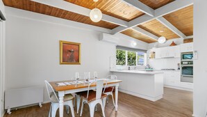 A modern kitchen with white cabinetry, a wooden dining table with white chairs, and a central island.