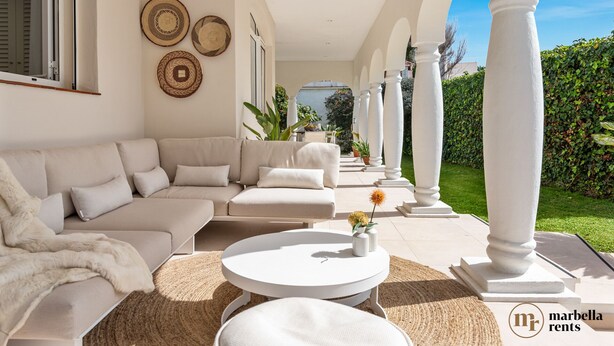 A modern living room with a beige sofa, a round coffee table, and a view of a garden through an open archway. - Beachfront Villa Casa Mosa | Ref. #32 (Marbella)