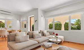 A modern living room with a beige sectional sofa, a round coffee table, and a view of a garden through large windows.