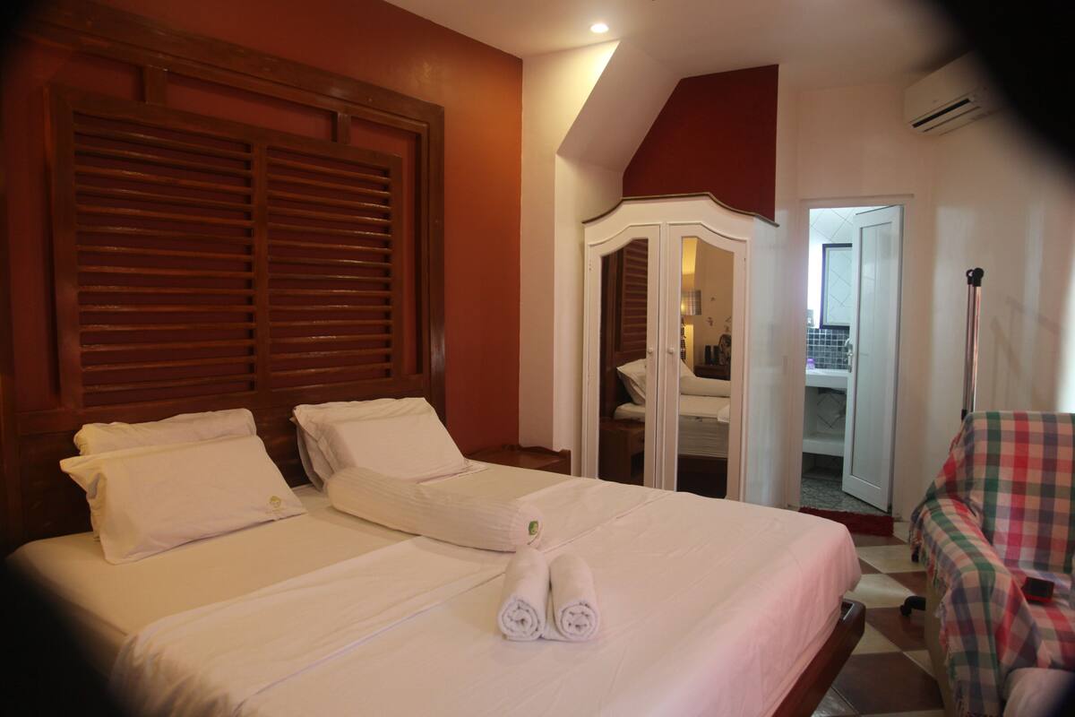 Habitación de hotel con dos camas, un armario y un sillón a cuadros.