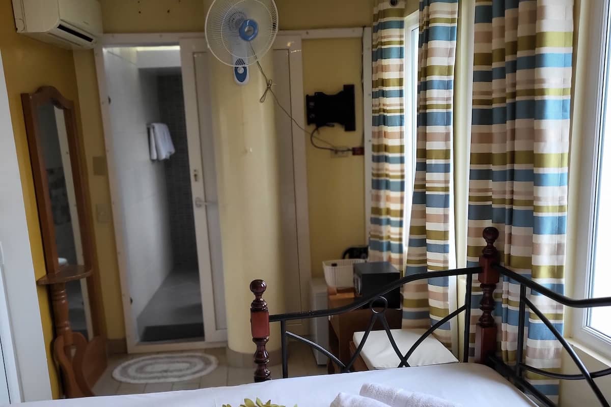 Habitación de hotel con cama, ventilador, escritorio y ventana con cortinas a rayas.