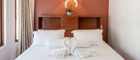 Une chambre d’hôtel avec un lit, une table de chevet, une lampe et une fenêtre avec des rideaux.