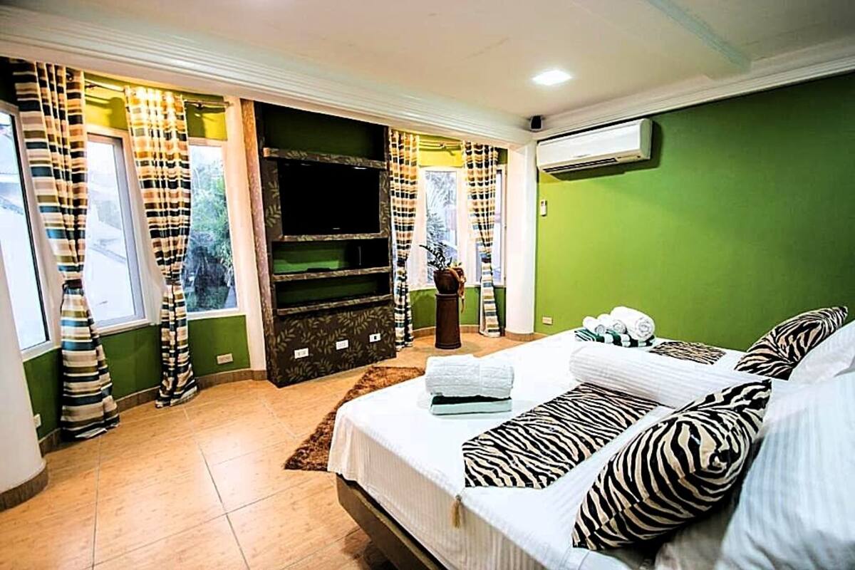 Un dormitorio con cama, cortinas, televisor de pantalla plana y aire acondicionado.