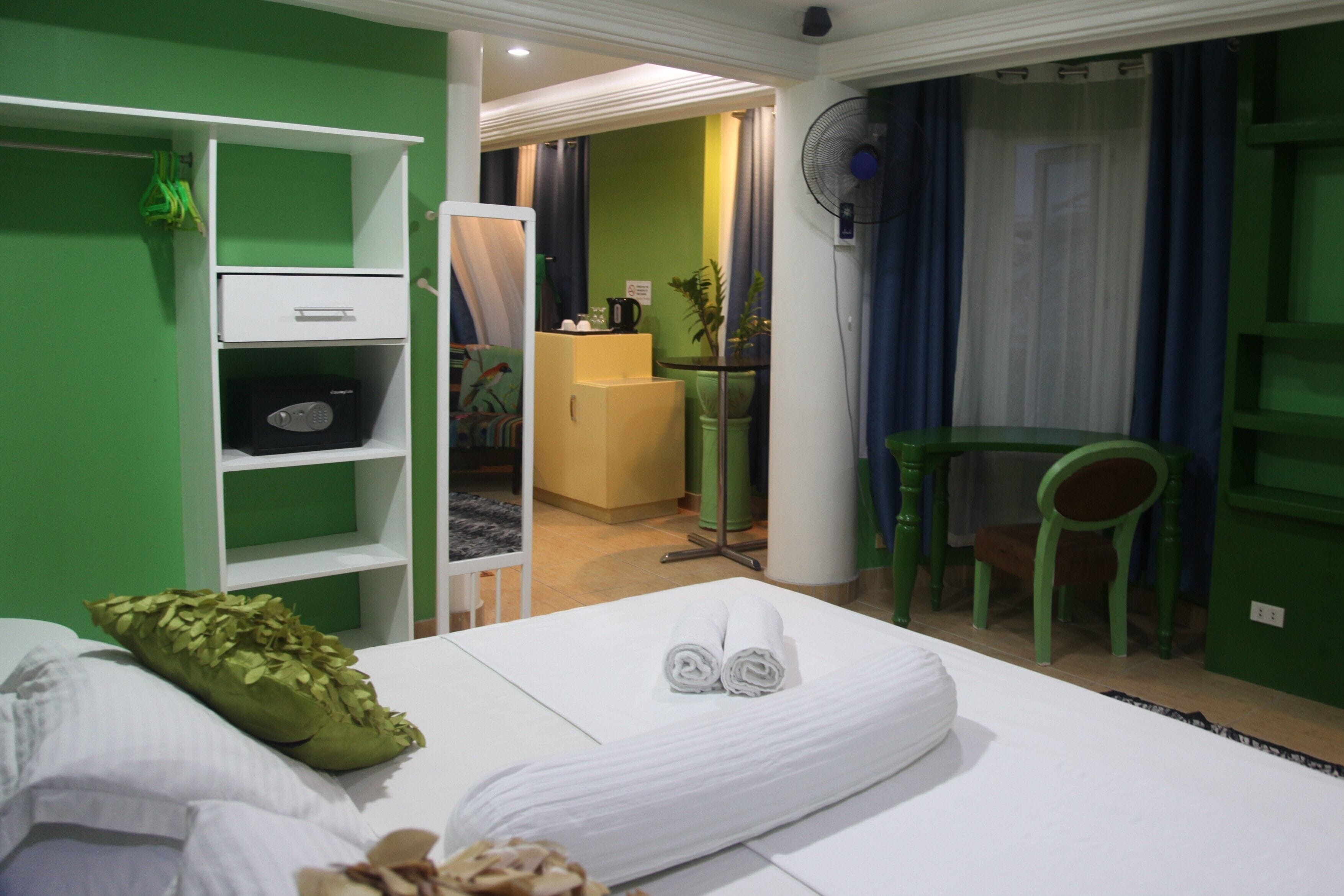 Een hotelkamer met een bed, een groene stoel, een bureau en een kleine kitchenette.