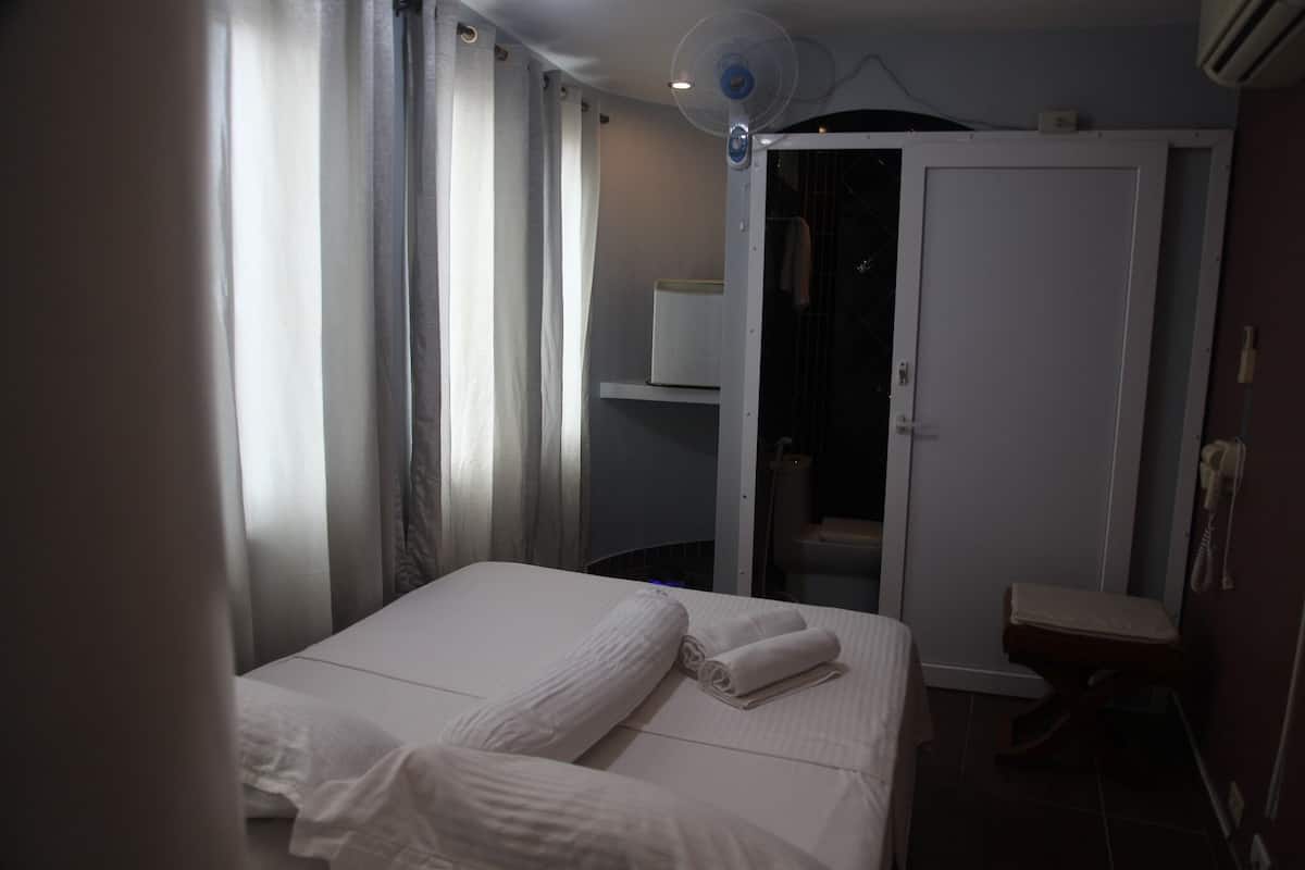 Habitación de hotel con cama, armario, mesita y ventilador de techo.