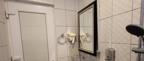 A bathroom with white tiled walls, a black sink, a mirror, a toilet paper holder, and a shower.