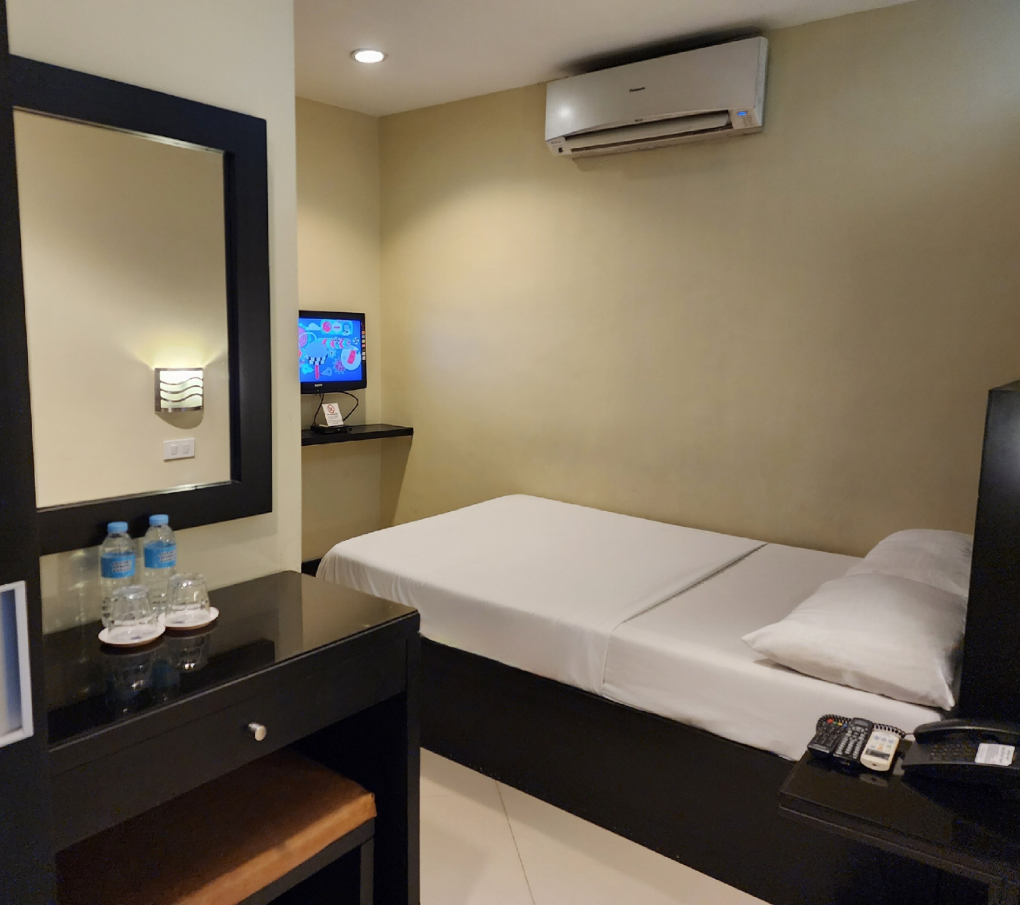 A hotel room with a bed, a desk with a mirror, a TV, and a minibar.