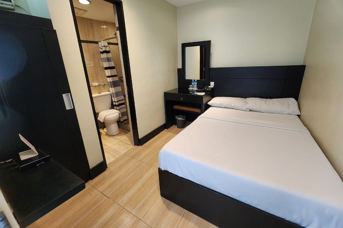 A hotel room with a bed, a bedside table, a mirror, and a bathroom visible through an open door.