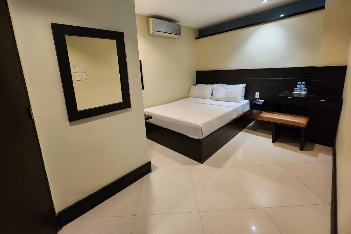 A hotel room with a bed, a desk, and an air conditioning unit.