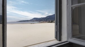 Blick aus einem Fenster auf einen Strand, im Hintergrund ein Berg.