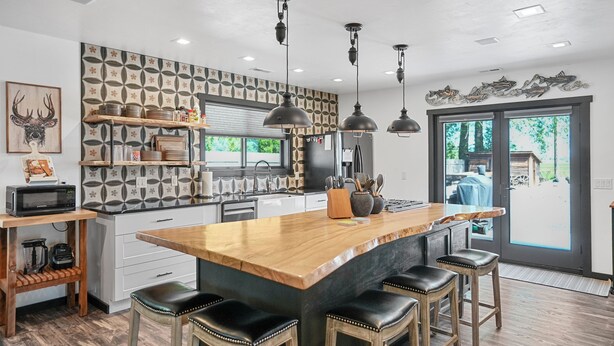 Una cucina moderna con una grande isola, sgabelli da bar, illuminazione a sospensione e un pannello decorativo.