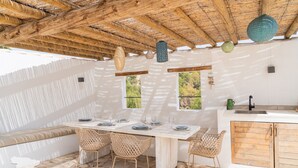 A dining area with a wooden table, wicker chairs, and a white bench. There are windows with views of greenery. - CostaBlancaDreams - Villa Etro in Benissa Costa (Benissa)