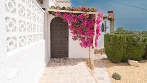 A white building with a brown door, a white wall with a geometric pattern, and a pergola with pink flowers. - CostaBlancaDreams - Villa Etro in Benissa Costa (Benissa)