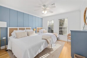 Une chambre avec deux lits, un ventilateur de plafond et une grande fenêtre avec des stores.