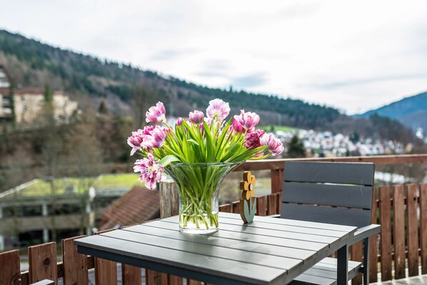Ein Tisch mit einem Blumenstrauß auf einem Balkon mit Blick auf eine Berglandschaft.
