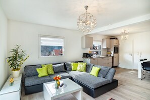 Ein modernes Wohnzimmer mit einer Eckcouch, einem Glastisch und einem Essbereich mit Tisch und Stühlen.