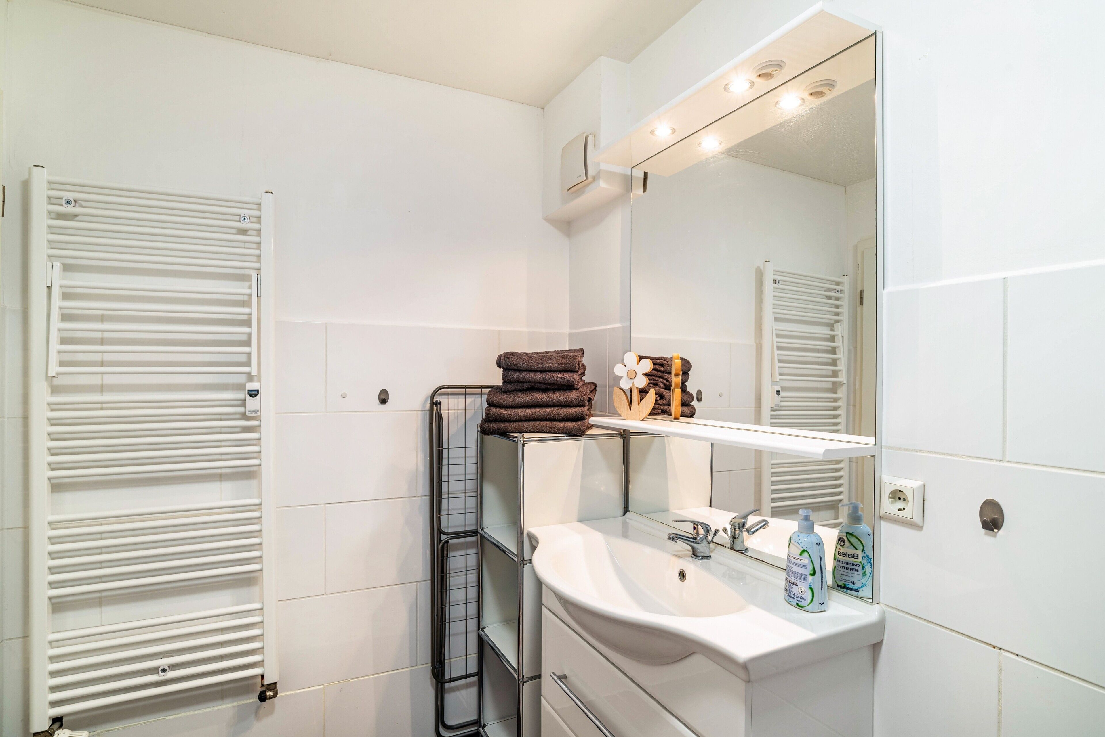 Un baño con lavamanos blanco, espejo, toallero y calentador de toallas.