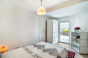 Ein Schlafzimmer mit Bett, Nachttisch mit Lampe, Kleiderschrank und Blick ins Freie.