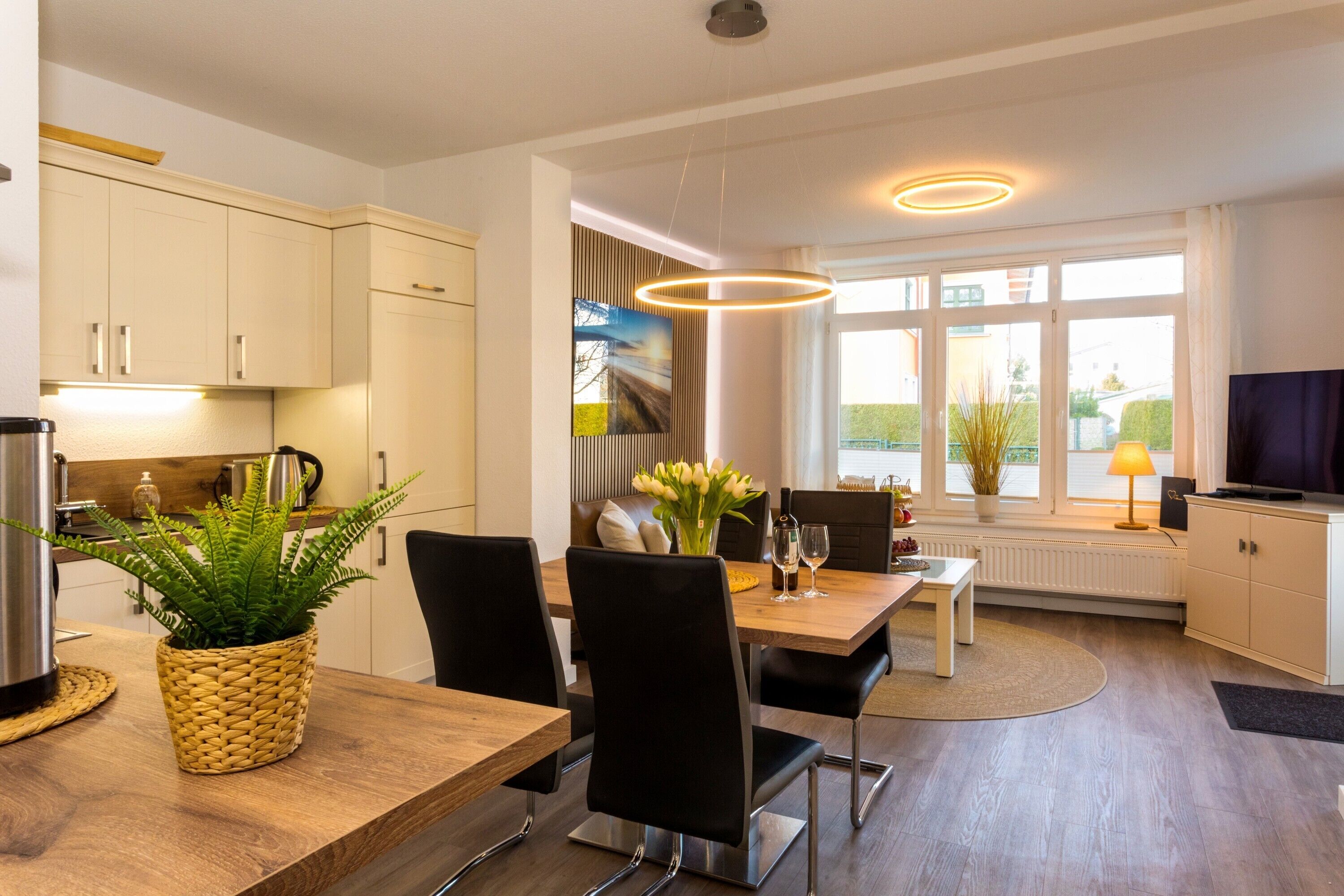 Een moderne keuken met witte kastjes, een eettafel met stoelen, een potplant en een televisie.