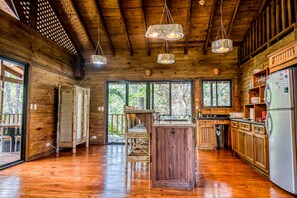 A spacious wooden cabin kitchen with large windows, a central island, and hanging pendant lights. - Rustic mountain-view home near the beach with private pool, deck, W/D, & WiFi (Dominical)