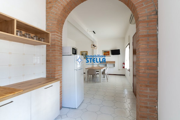 A kitchen with a wooden countertop, white cabinets, a refrigerator, and a brick archway.