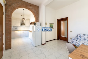 A kitchen with white cabinets, a refrigerator, and a brick archway leading to another room.