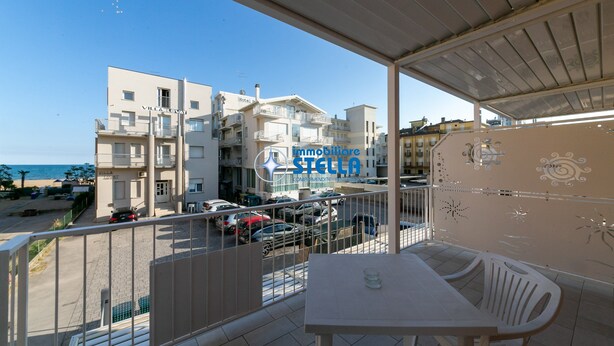 Ein Balkon mit Tisch und Stühlen, der auf eine Straße mit parkenden Autos und Gebäuden blickt.