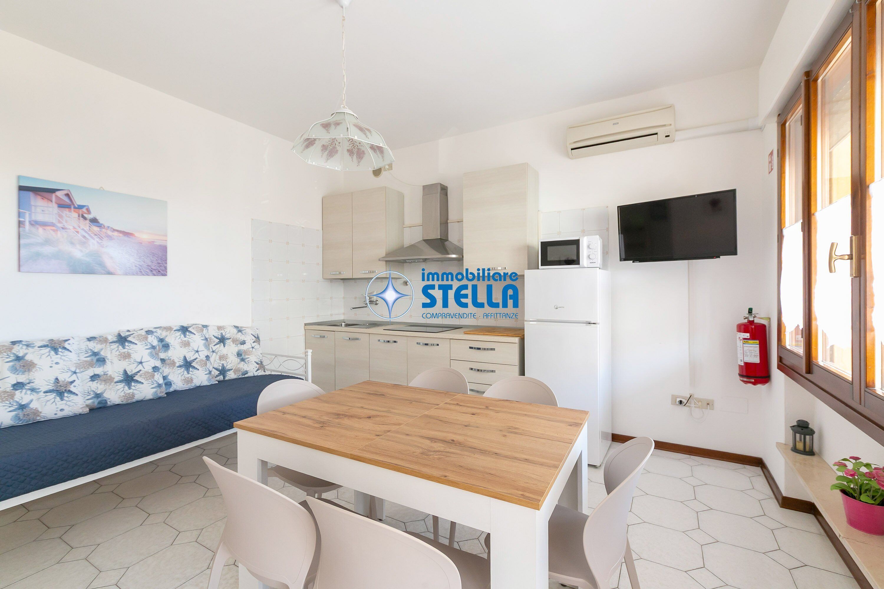 A modern kitchen with a wooden table and chairs, a sofa, and a mounted TV.
