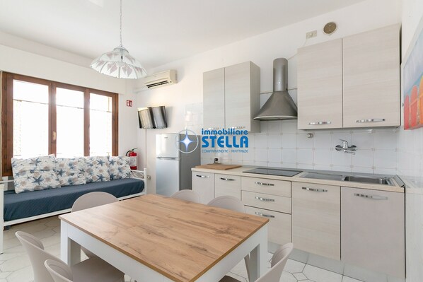 A modern kitchen with a dining area, a sofa, and a TV.