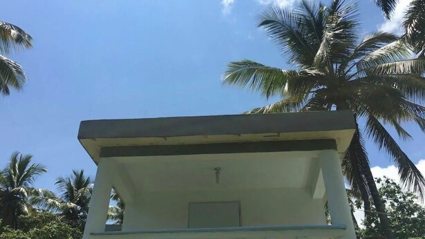 A white building with a balcony and a door, surrounded by palm trees. - Relaxing Beachfront Apartment steps to the beach (las pascualas)