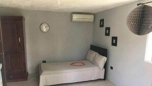 A small, single-bed room with a wooden door, an air conditioning unit, a clock, and a wall-mounted light fixture. - Relaxing Beachfront Apartment steps to the beach (las pascualas)