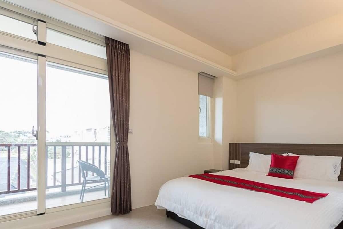 A hotel room with a large bed, a window with curtains, a balcony, and a view of the outside.
