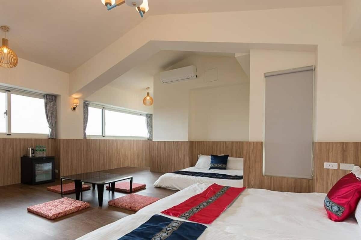 A modern hotel room with a loft-style ceiling, a large bed with decorative pillows, a desk with a chair, and a small kitchenette.