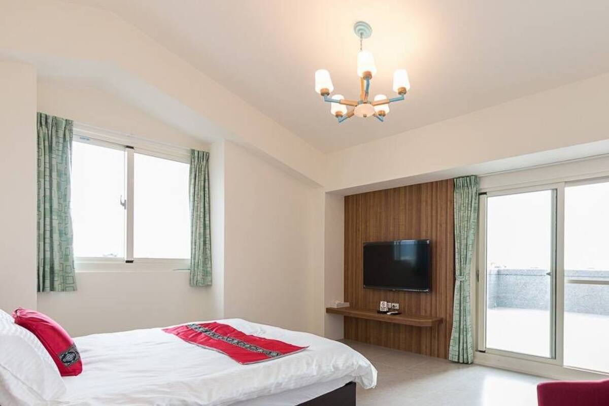 A hotel room with a bed, a TV, a sliding door to a balcony, and a red chair.