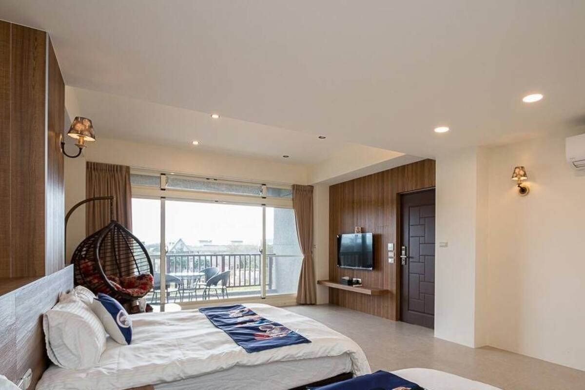A modern hotel room with a bed, a TV, a balcony with a view, and a wooden wall.