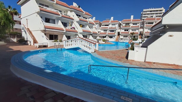 Une piscine entourée d’immeubles à plusieurs étages dotés de balcons, un ciel dégagé et un numéro de piscine clairement visible.