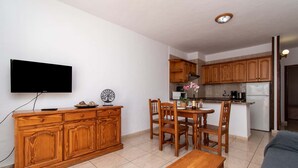 Un espace de vie compact comprenant une table à manger en bois, un téléviseur fixé au mur et un coin cuisine.